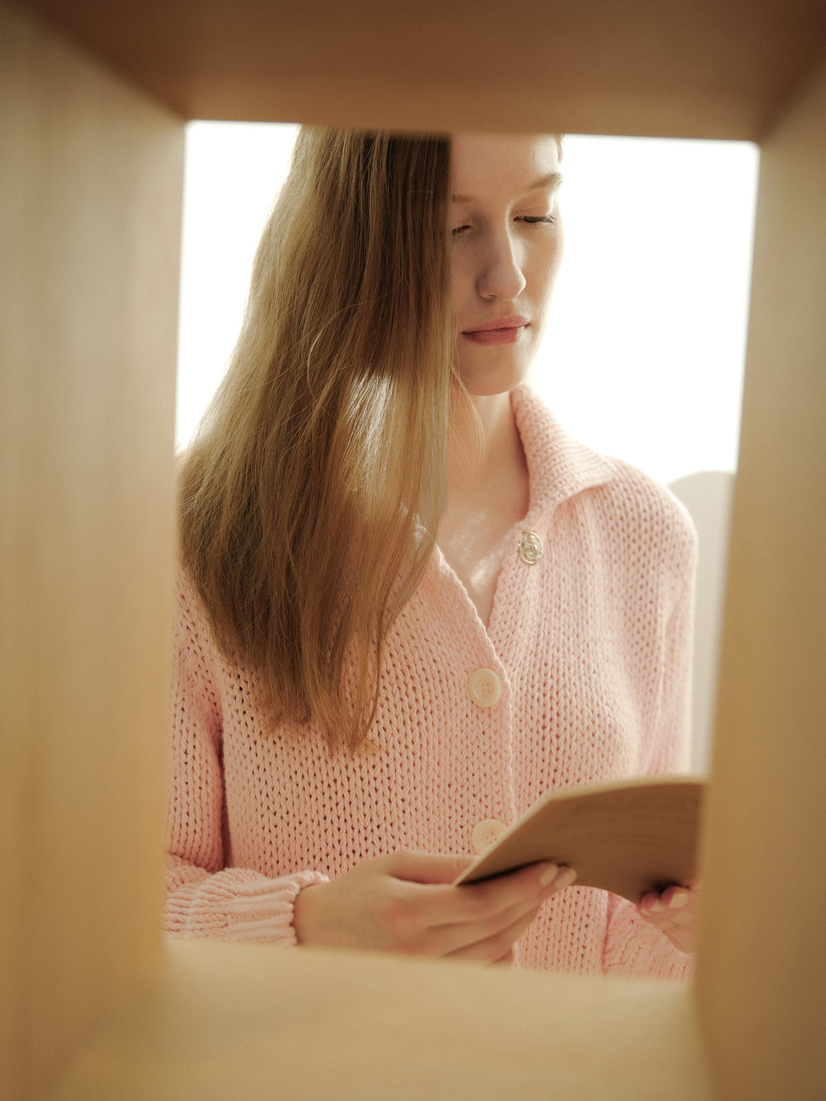 Mujer con a pink knit cardigan with large white buttons holding a small notebook.