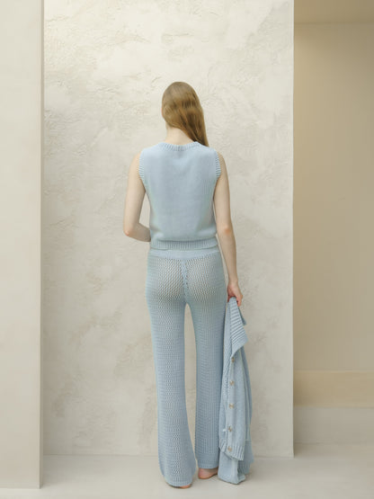 Back view of a donna con a azzurro top in maglia senza maniche e matching wide knit pants, holding a azzurro pallido cardigan.