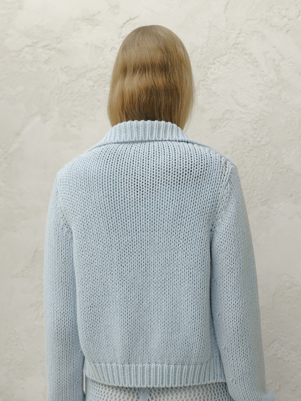 Back view of a modella con a azzurro chunky knit bomber jacket con a ribbed collar e hem.