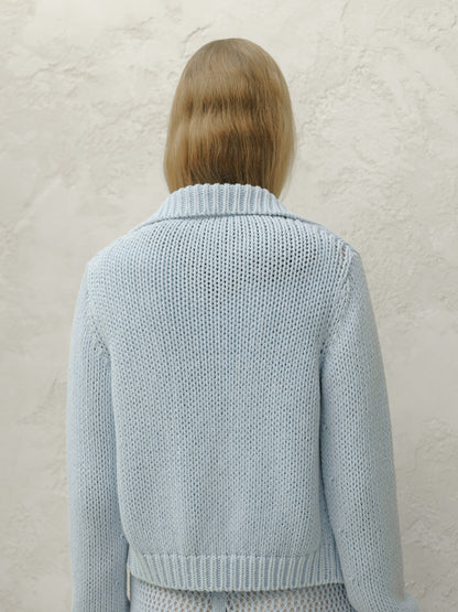 Back view of a modella con a azzurro chunky knit bomber jacket con a ribbed collar e hem.