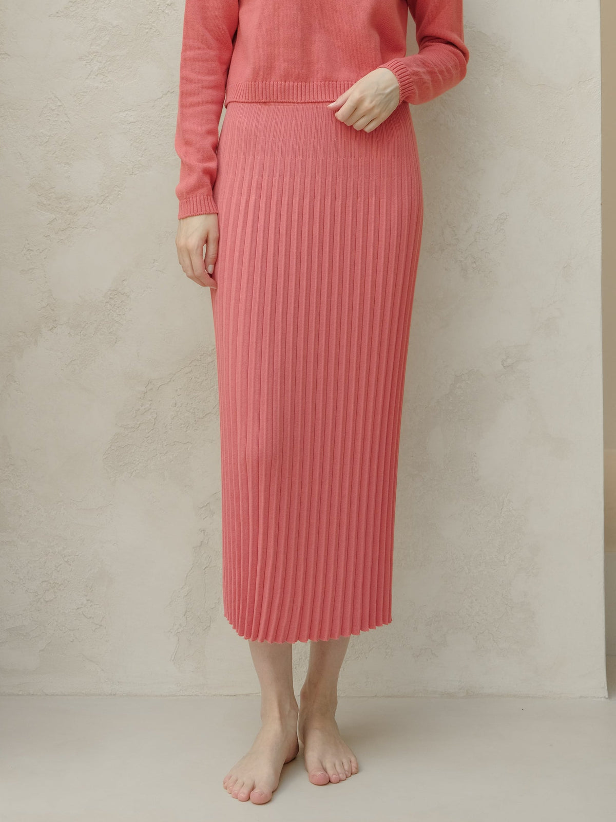 Person wearing a pink ribbed knit skirt and sweater against a beige background