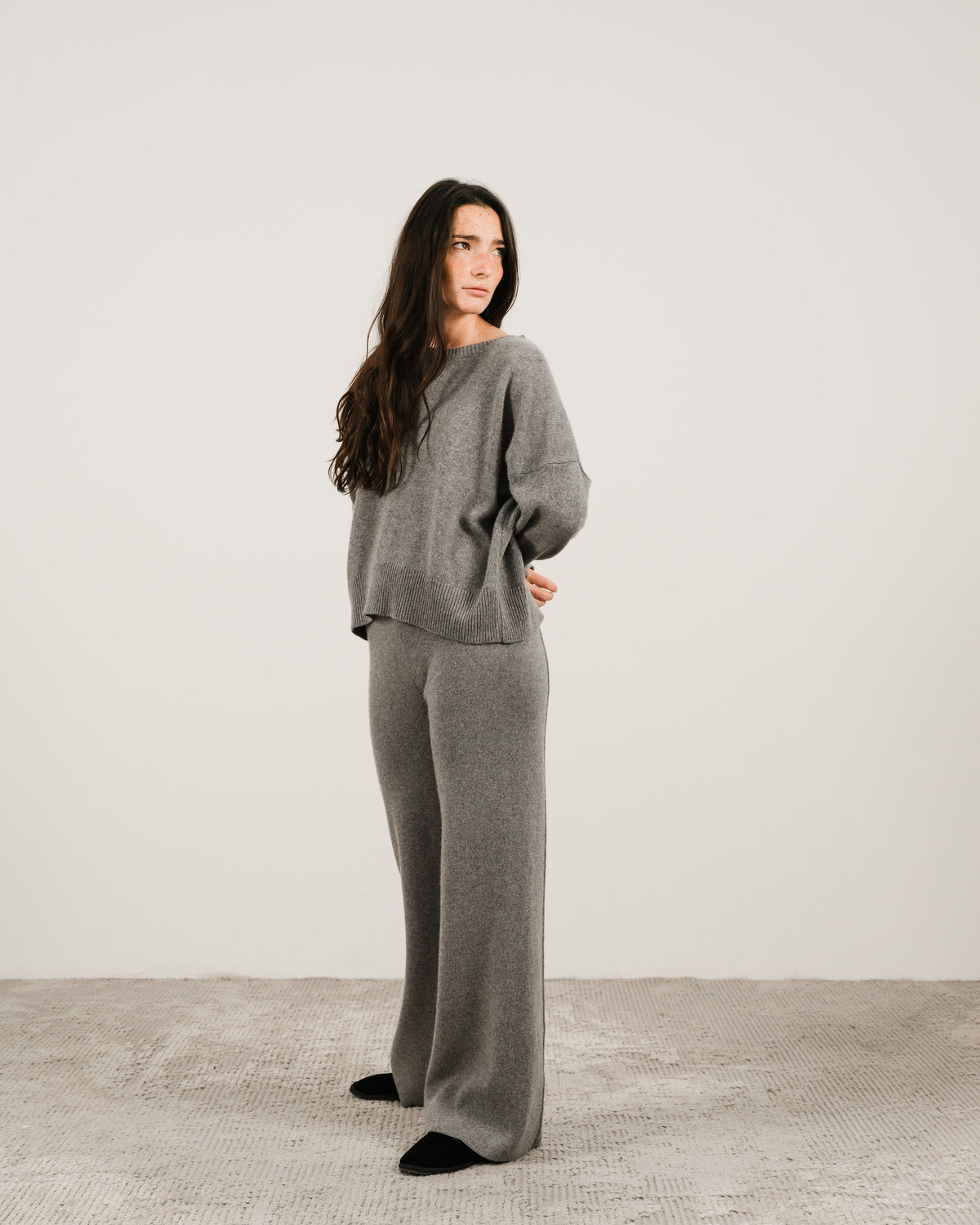 Woman in grey cashmere mix crewneck sweater with matching wide-leg pants standing in a studio setting.