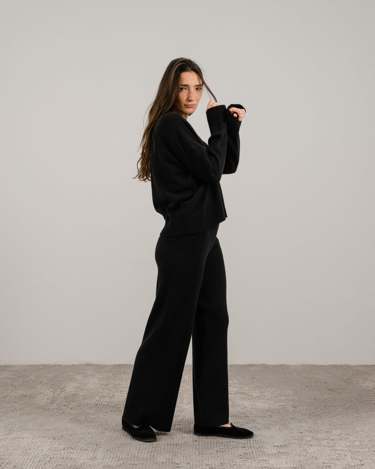 Full body side view of a woman in a black cashmere mix crewneck sweater with wide-leg pants