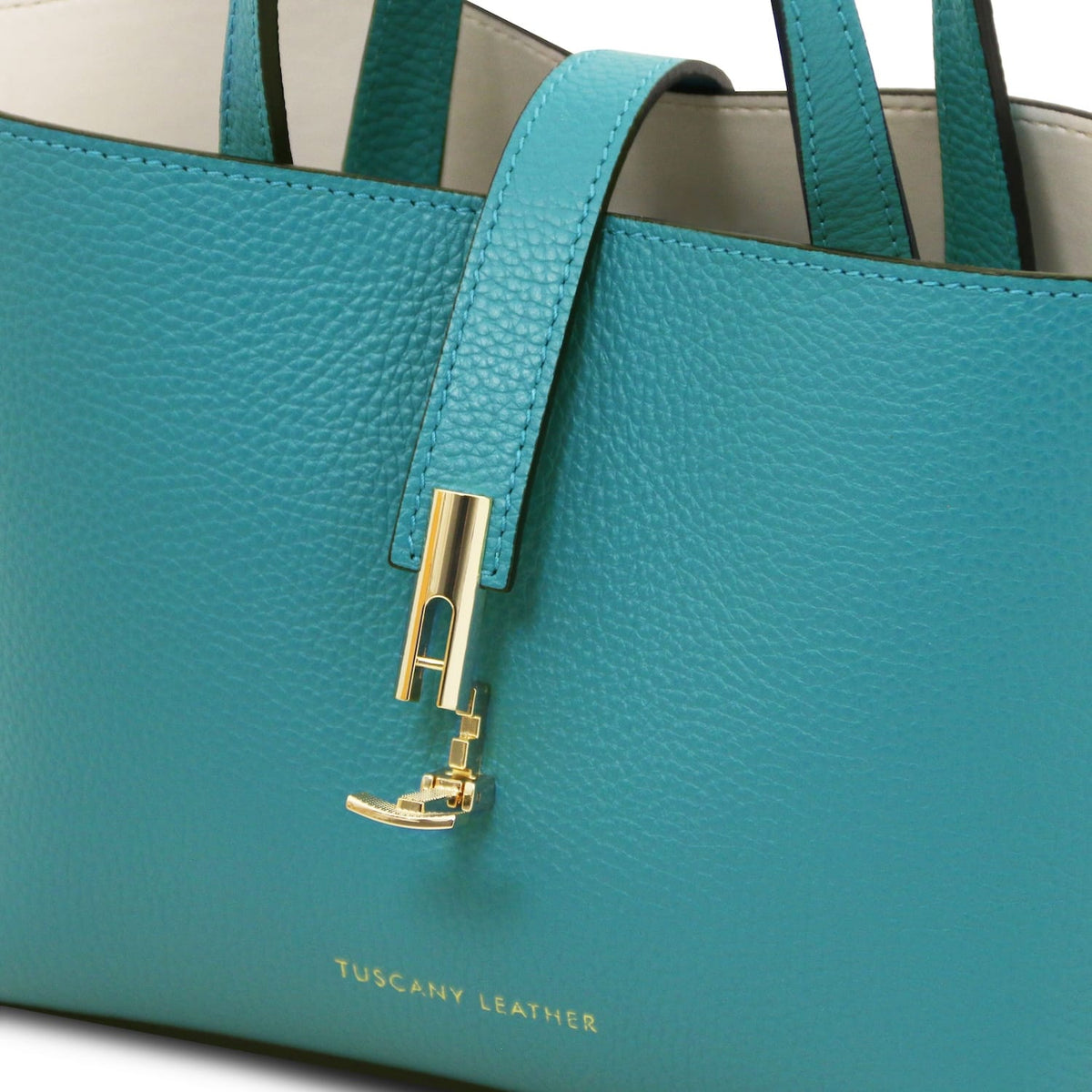 Close-up of teal pebbled leather tote purse with gold-toned hardware and Tuscany Leather embossed branding detail.