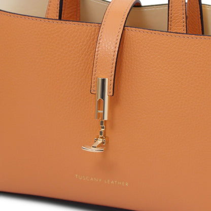 Close-up of tan pebbled leather tote with gold hardware and embossed "Tuscany Leather" branding on smooth leather surface.