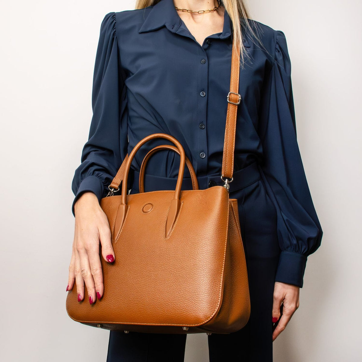 Camelia Italian leather tote in tan with two top handles and an adjustable shoulder strap held by a model in a navy blouse