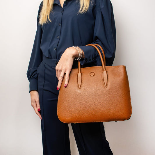 Cuero piel granulada Camelia tote with double handles, carried by a woman in a azul marino outfit.
