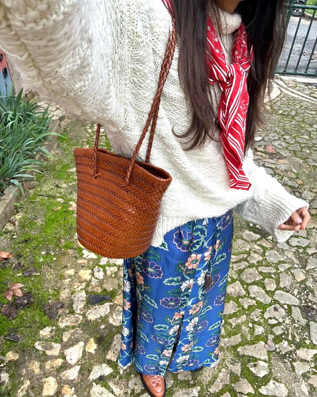 Carmel hand woven brown leather shoulder bucket bag worn on the shoulder with a braided strap, combinada com a cream knit sweater and red scarf.