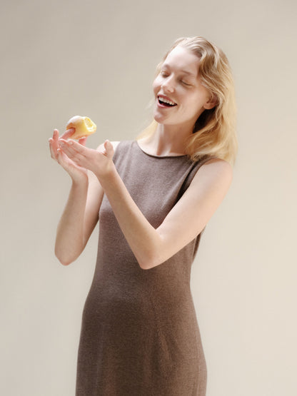 Modella con warm marrone cashmere blend boat neck sleeveless dress smiling while holding a pastry
