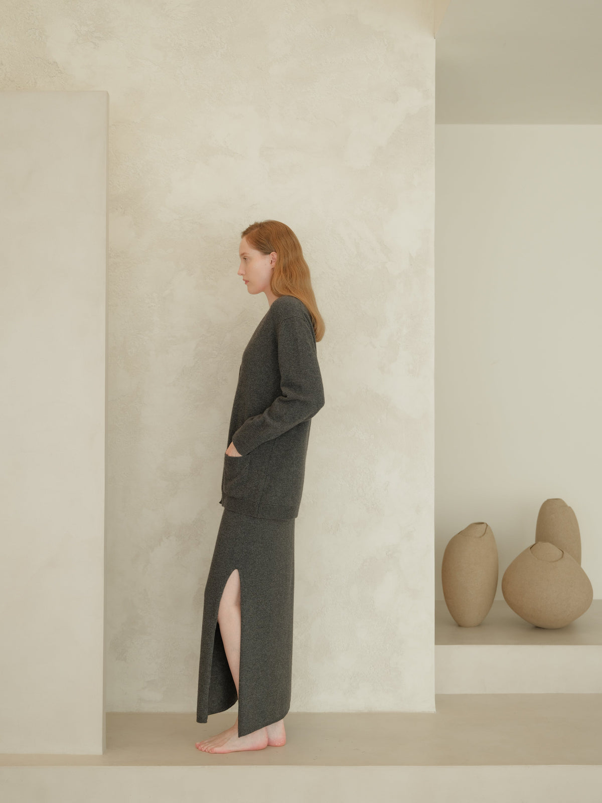 Side view of a woman wearing a dark gray cashmere blend high-waist long knit skirt with a side slit
