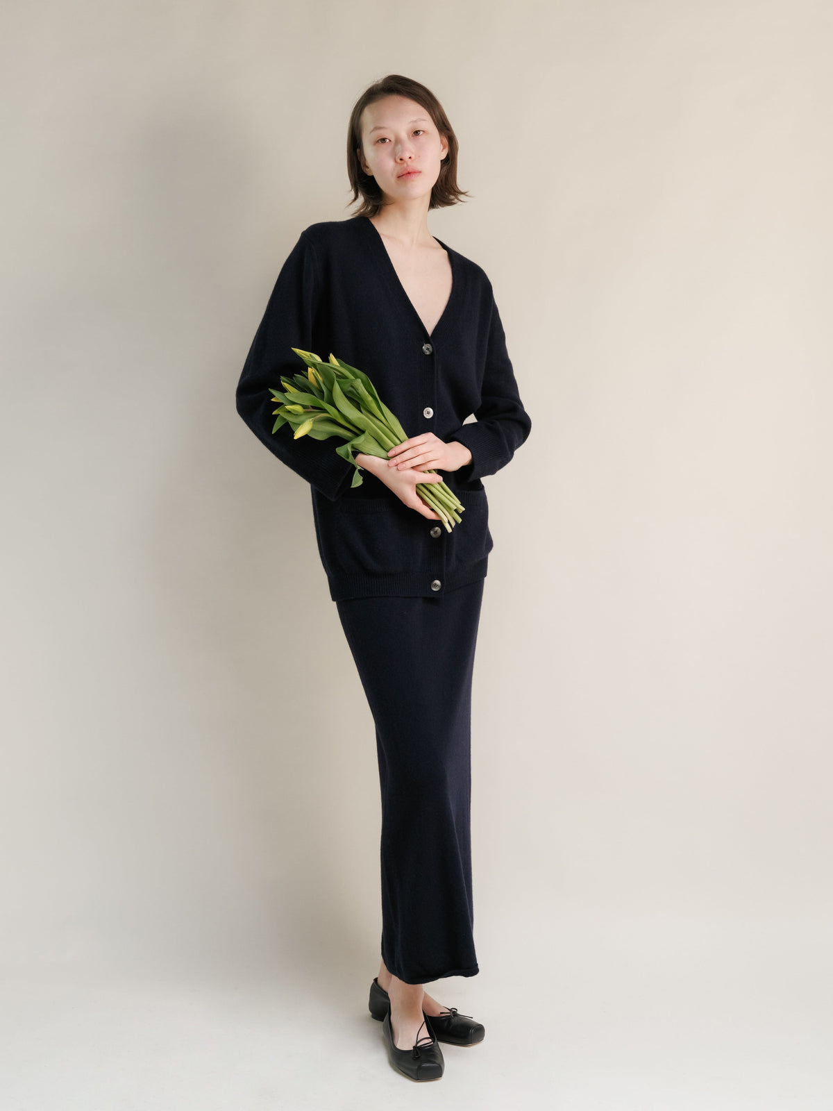 Model in navy cashmere blend cardigan and coordinating long skirt, holding a bouquet of flowers
