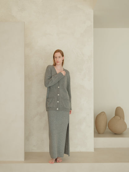 Front view of a woman in a gray knit cardigan with white buttons over a matching long skirt that features a front slit in a minimalist studio.