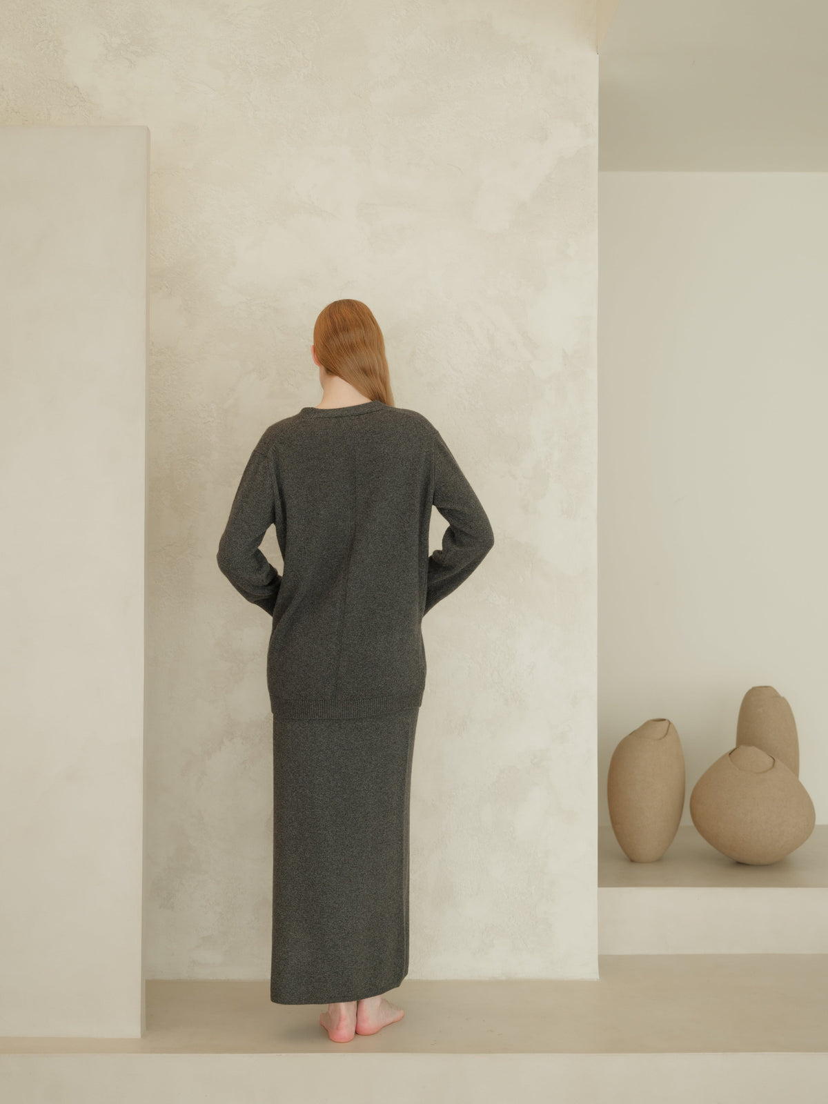 Back view of a woman wearing a dark gray cashmere blend high-waist long knit skirt and a matching oversized cardigan