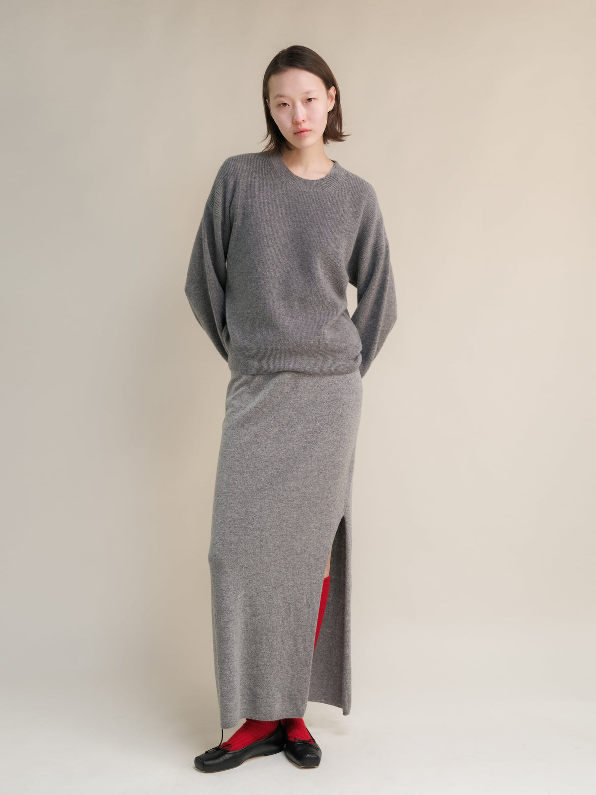 Model wearing gray cashmere blend high-waist long skirt with a side slit and a matching knit top