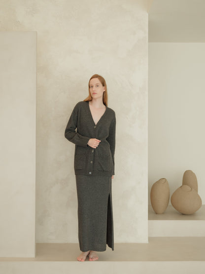 Back view of a woman in a dark gray cashmere blend cardigan with buttons over a matching high-waist long knit skirt with a side slit