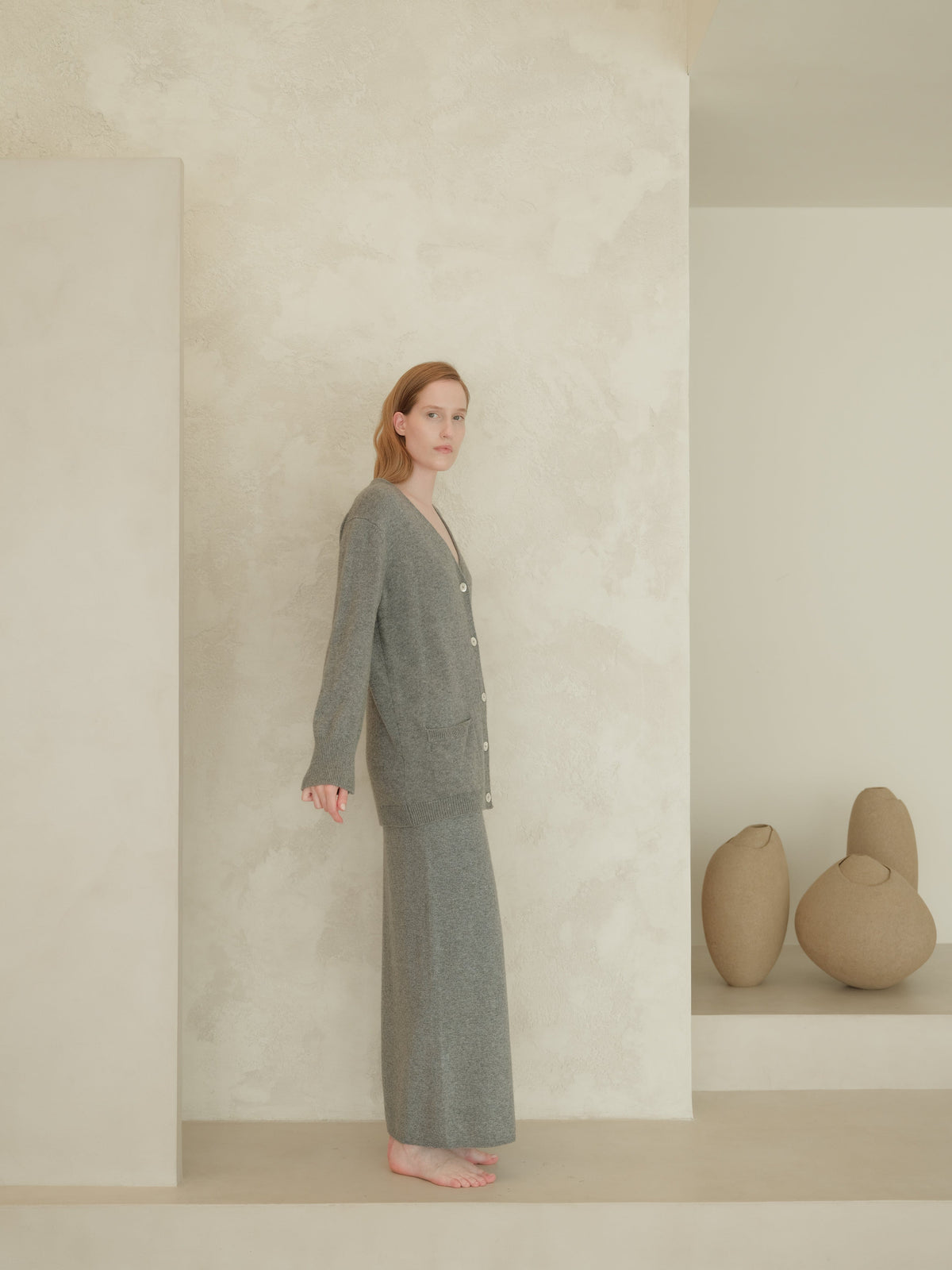 Side view of a model wearing a grey knit cardigan with a long grey cashmere blend skirt featuring a side slit