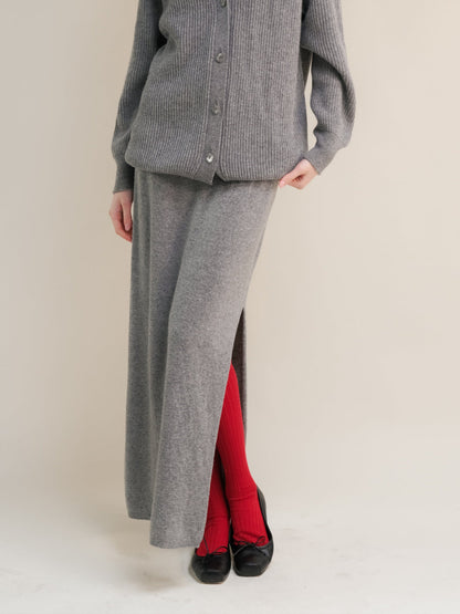 Close-up of a grey knit skirt with a side slit worn over red tights and black flats