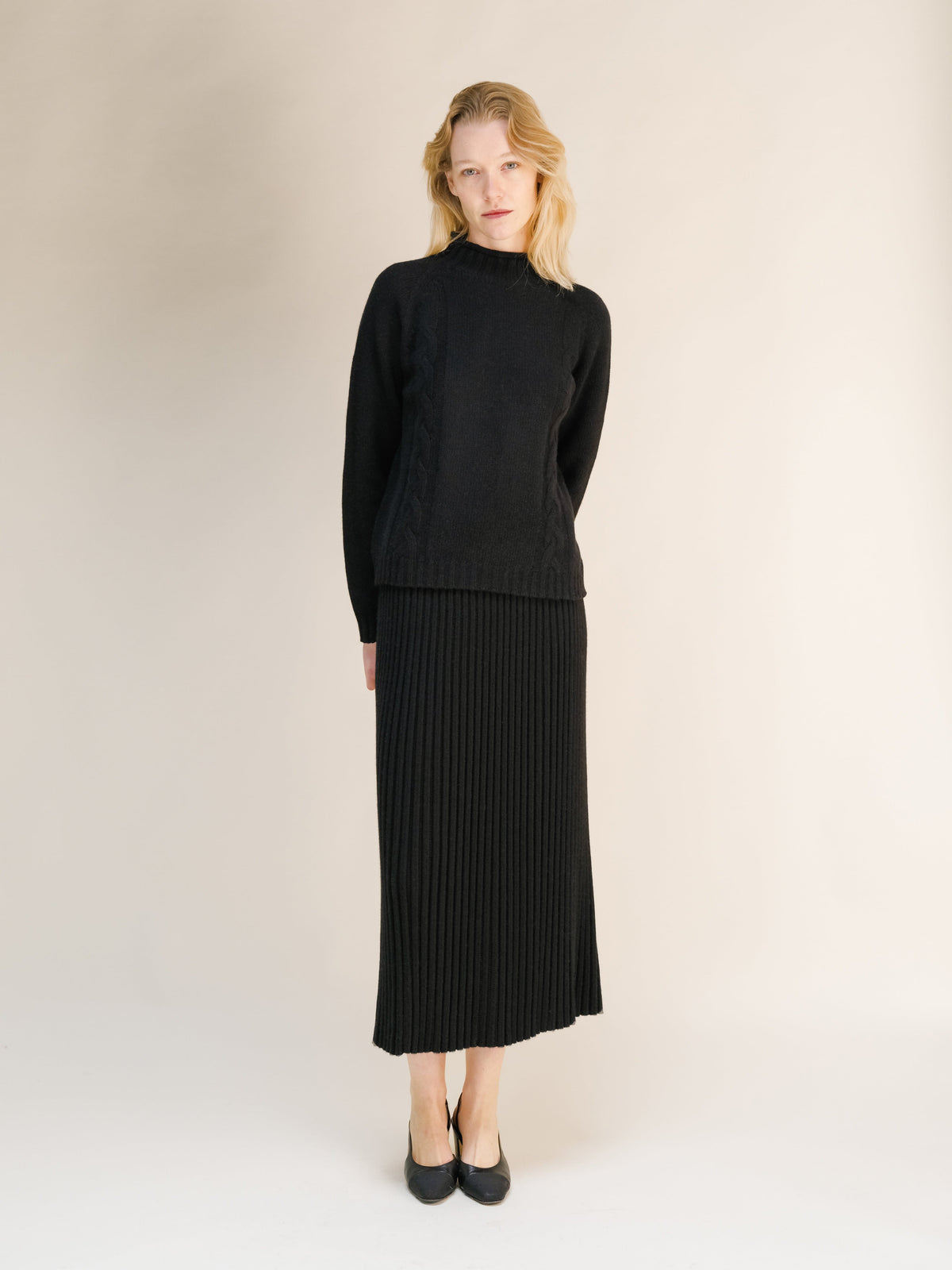 Front view of a model wearing a black cashmere blend perforated 3D knit skirt with a matching sweater