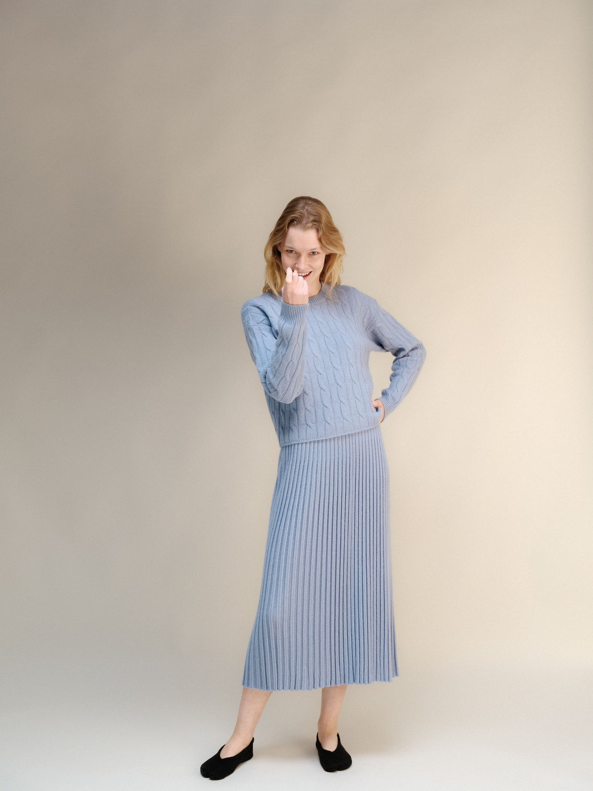 Model wearing pale blue cashmere blend cable knit sweater with a matching ribbed midi skirt.