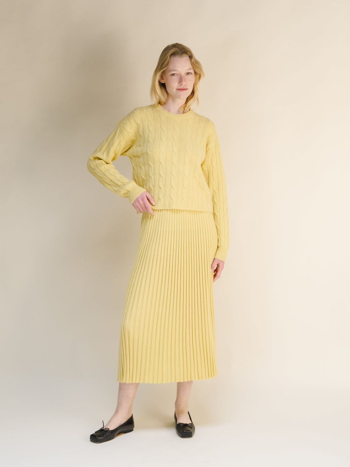 Model wearing pale yellow cashmere blend 3D knit sweater with matching ribbed midi skirt and black flats