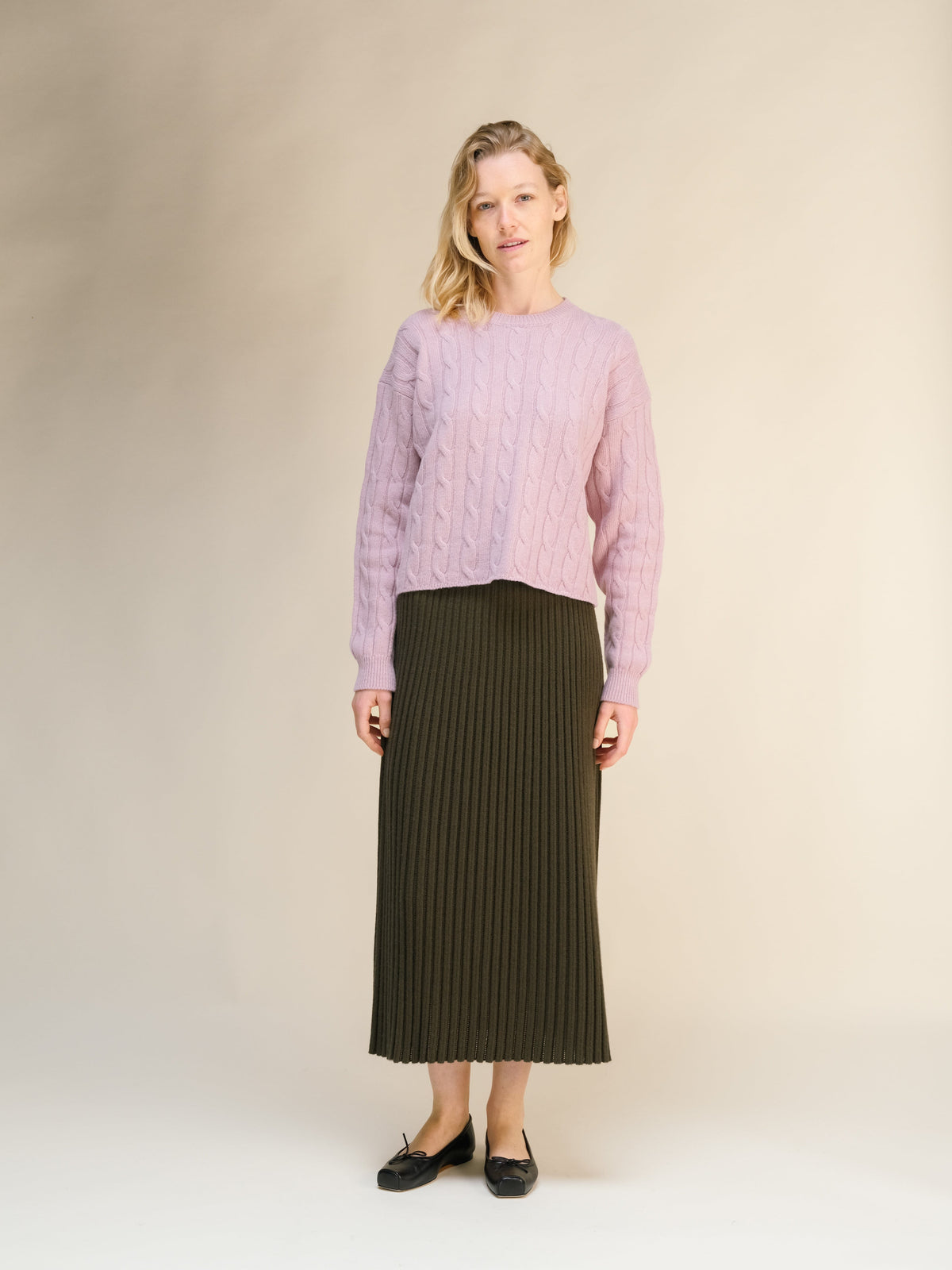 Model wearing a pink cable knit sweater with a dark olive ribbed midi skirt from the cashmere blend 3D knit collection