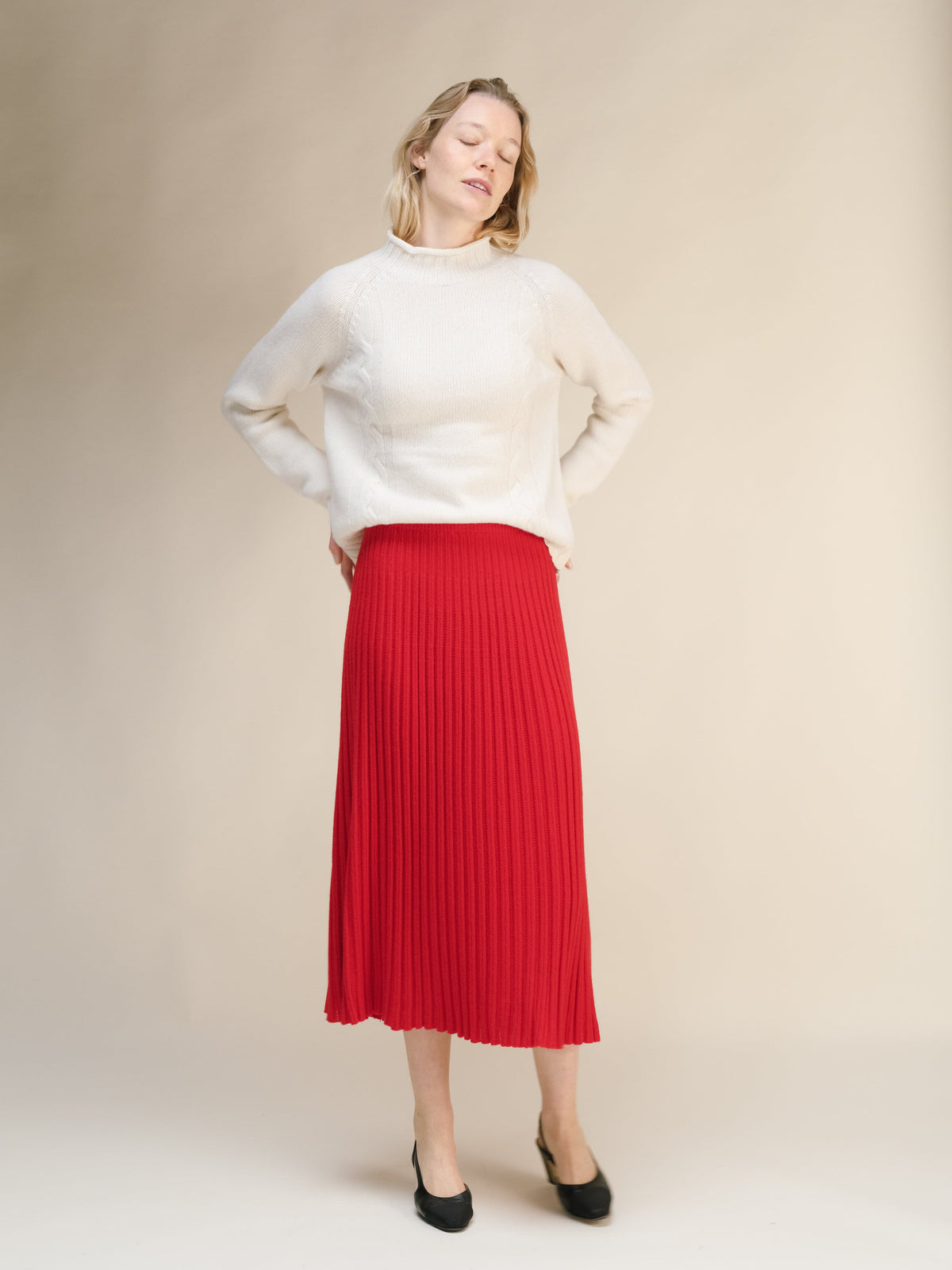 Full-length view of a model wearing a cream knit sweater with a red ribbed midi skirt and black heels.