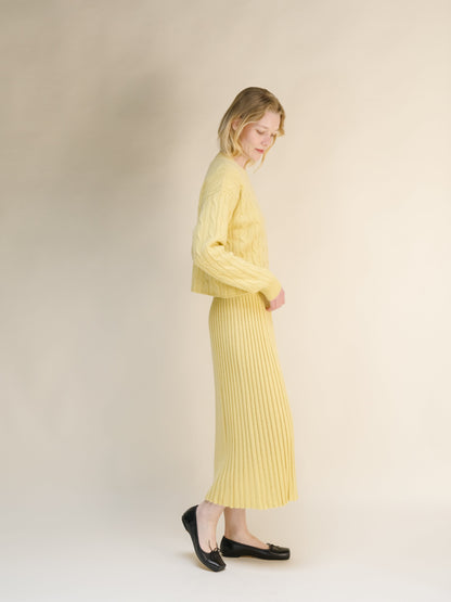 Side view of a woman wearing a pale yellow cashmere blend knit skirt with a matching sweater against a neutral backdrop.