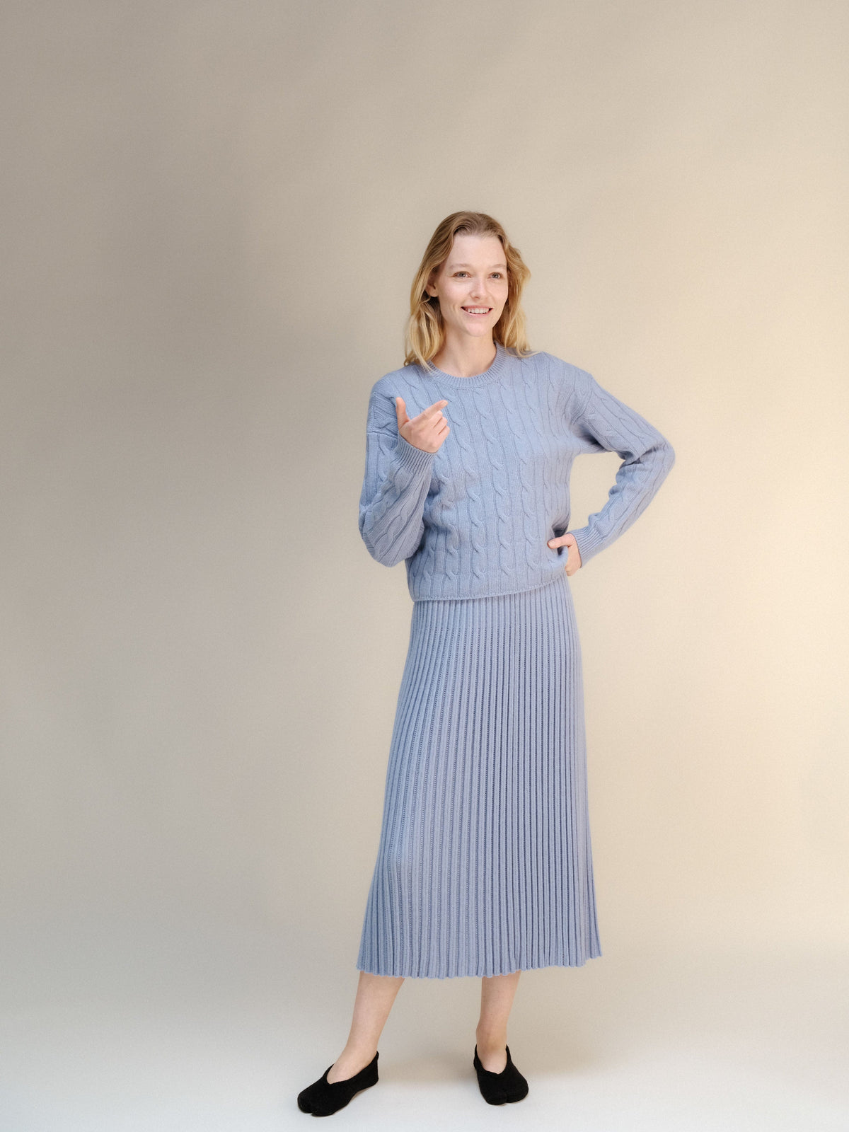 Model wearing a powder blue knit sweater with a matching ribbed midi skirt in a neutral studio.
