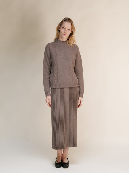 Model wearing a taupe cashmere blend knit sweater and matching long ribbed skirt against a neutral backdrop.