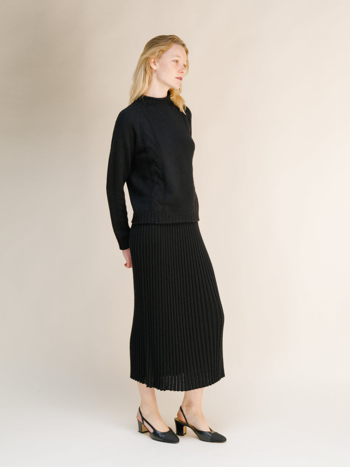 Side view of a model in a black cashmere blend perforated 3D knit skirt paired with a coordinating knit sweater