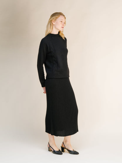 Side view of a model in a black cashmere blend perforated 3D knit skirt paired with a coordinating knit sweater