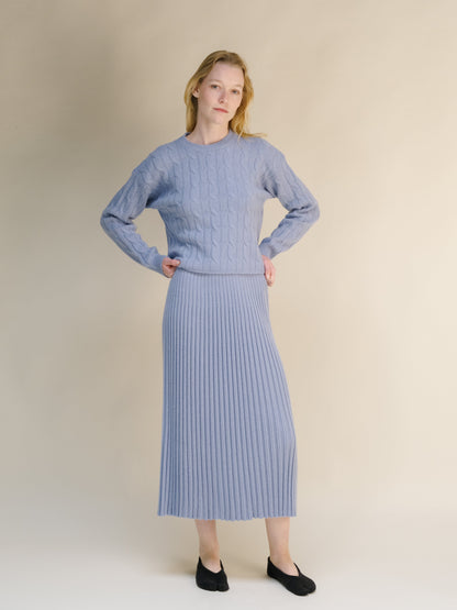 Model in pale blue cashmere blend knit set standing with hands on hips against beige backdrop.