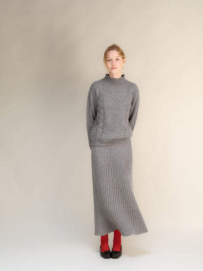 Model wearing gray cashmere blend 3D-knit ribbed maxi skirt with a matching sweater against a neutral backdrop