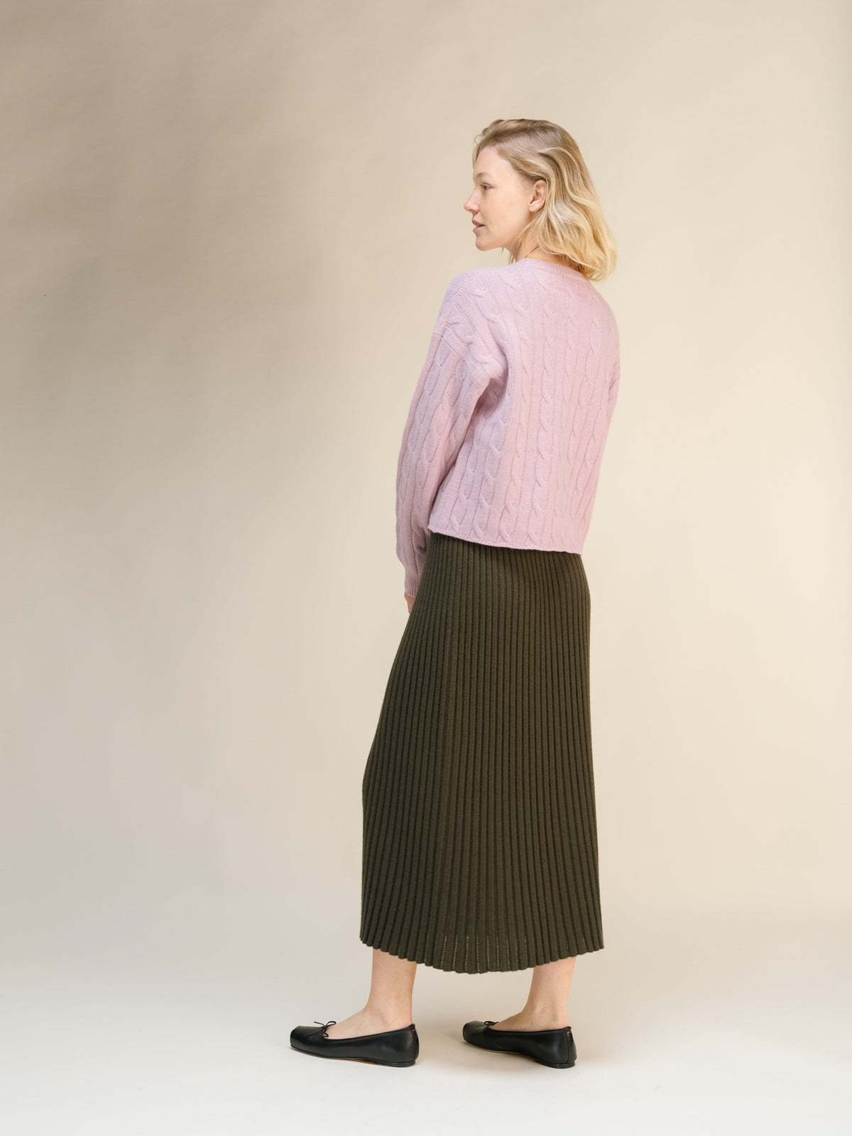 Side view of a model wearing a pink knit sweater and olive ribbed midi skirt