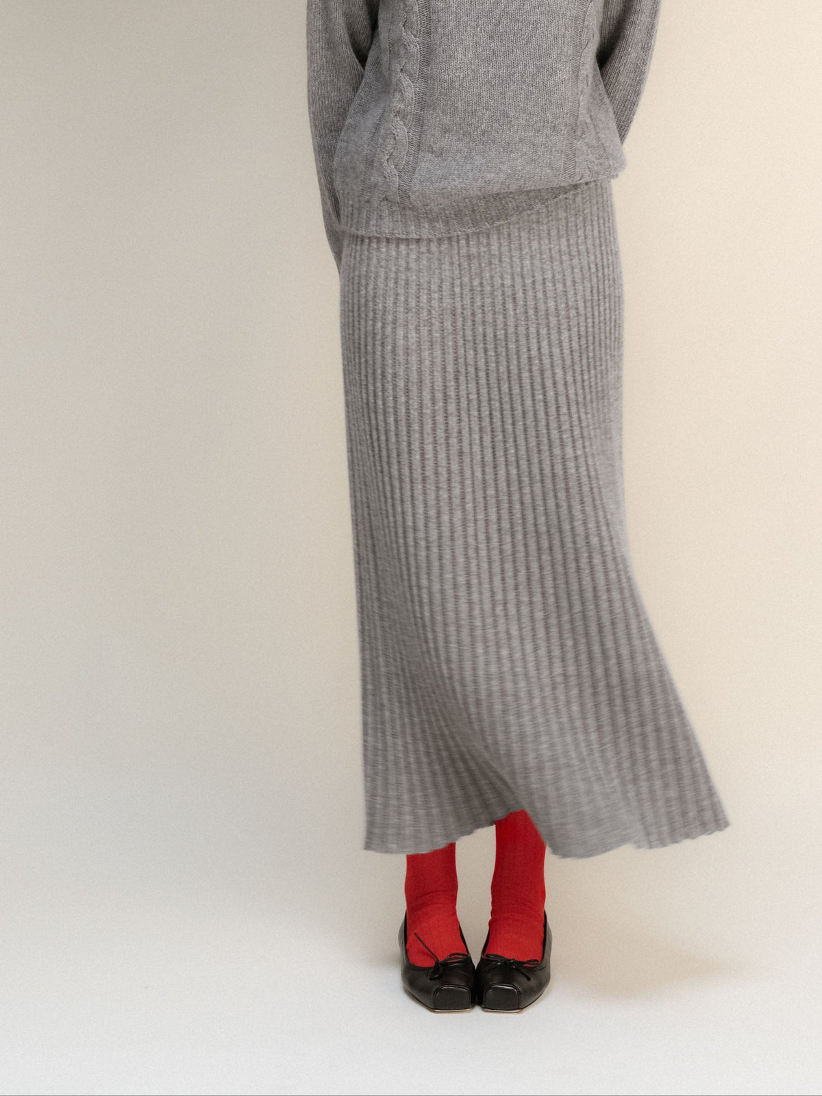 Gray cashmere blend 3D knit maxi skirt with a ribbed hem, paired with red socks and black flats.