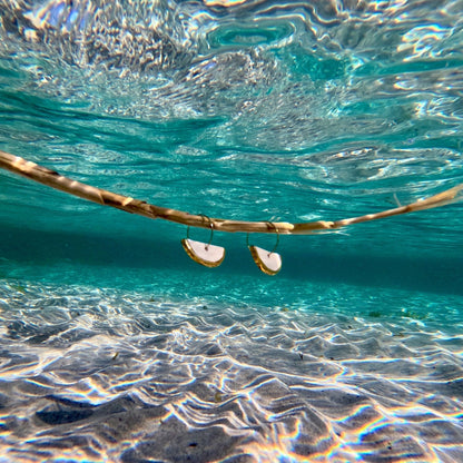 Orecchini in ceramica con bordi dorati nell’acqua azzurra limpida sopra un fondale sabbioso