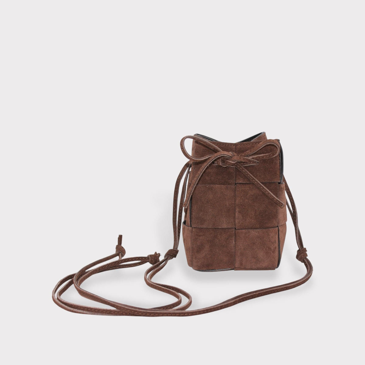 brown suede leather bucket bag with woven panel design and cierre de cordón on light gray background