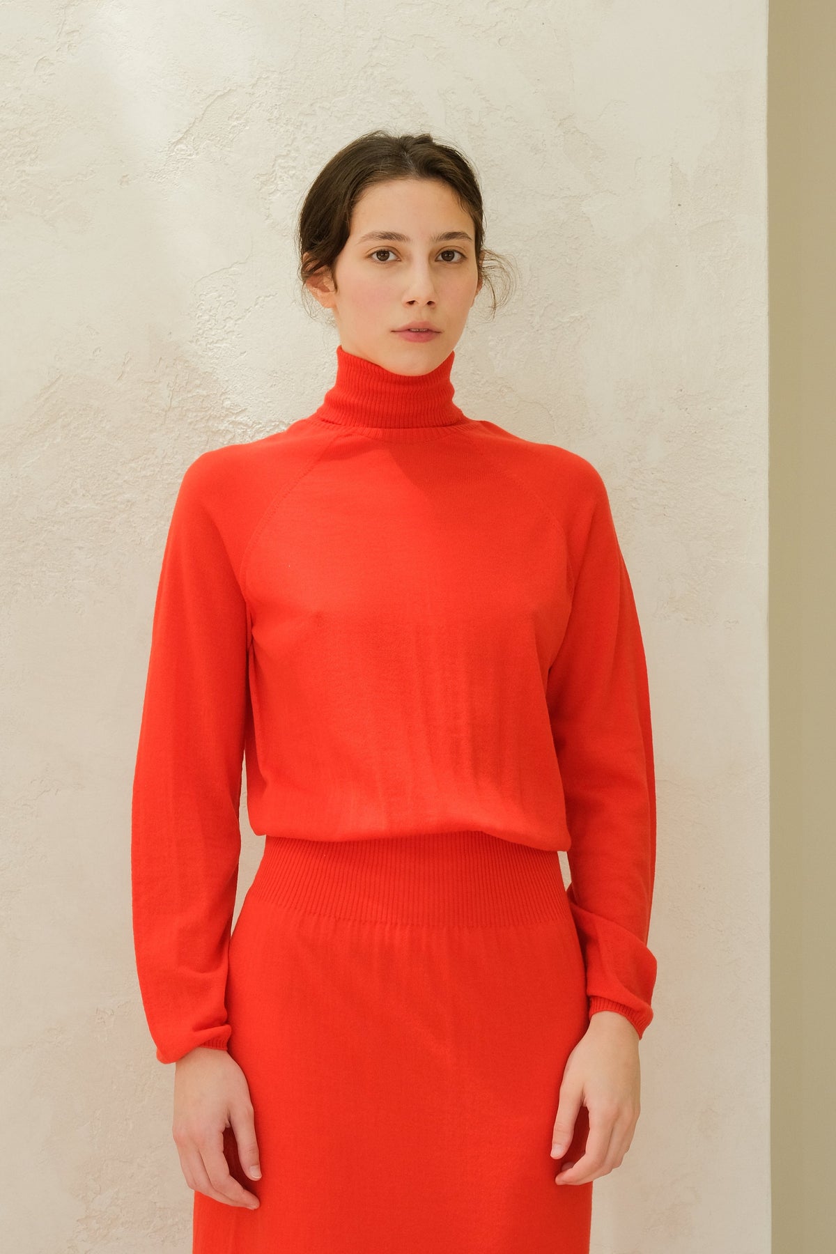 Close-up of a model in a bright red 3D knit merino wool turtleneck sweater with long sleeves.