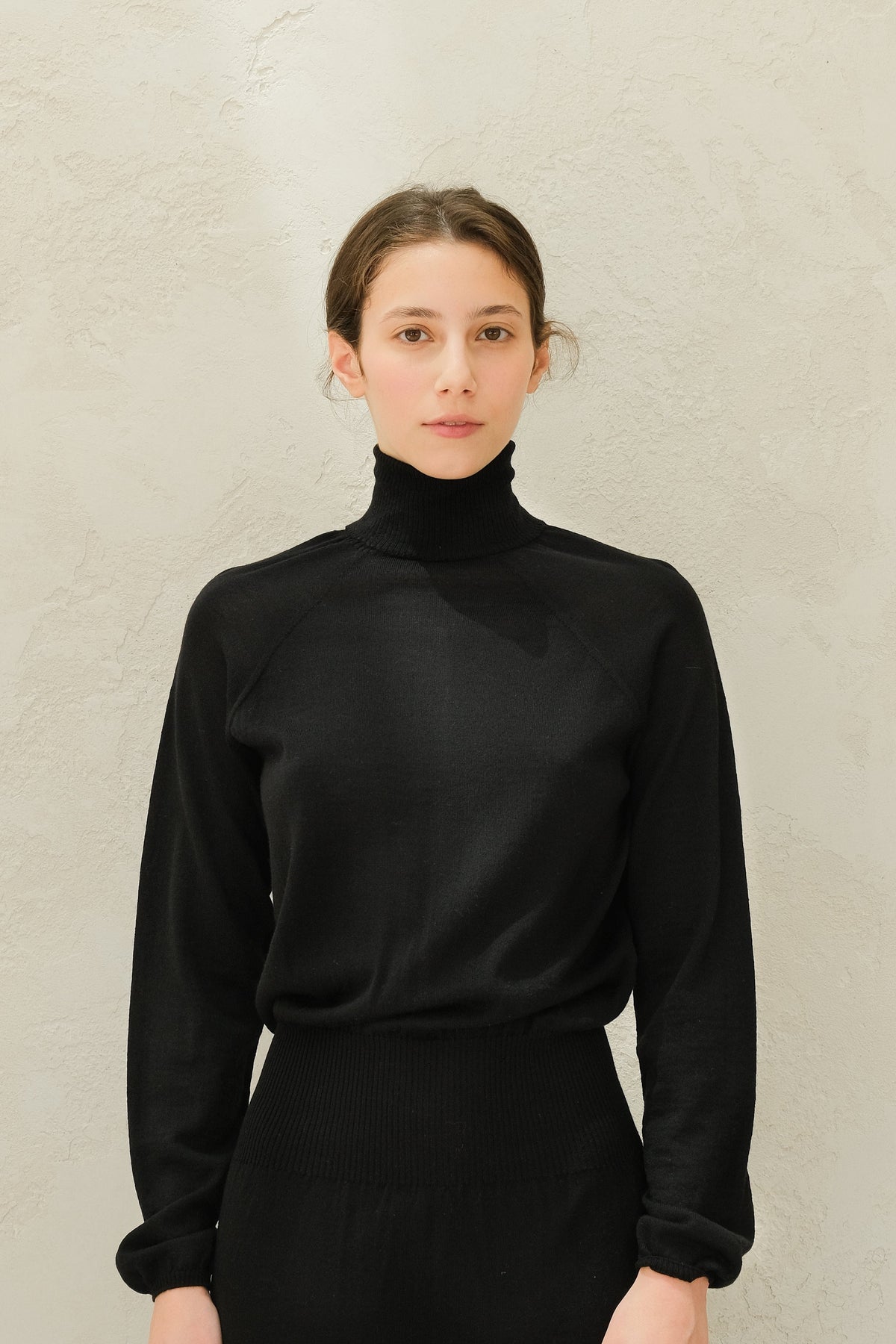 Close-up of a model wearing a black 3D-knit merino wool turtleneck sweater.