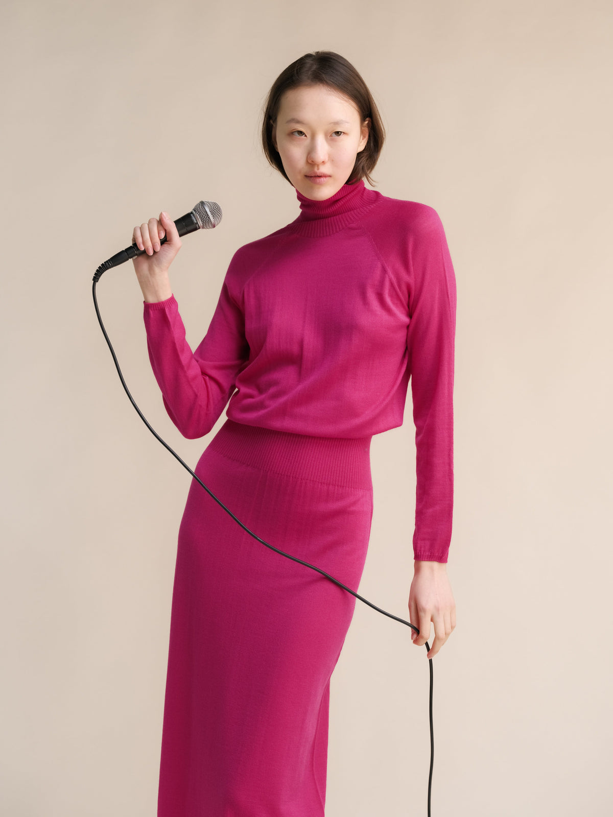 Model wearing magenta 3D knit merino wool dress posing with a microphone in a studio