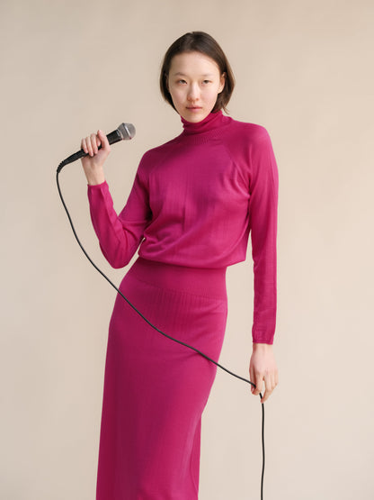 Model wearing magenta 3D knit merino wool dress posing with a microphone in a studio