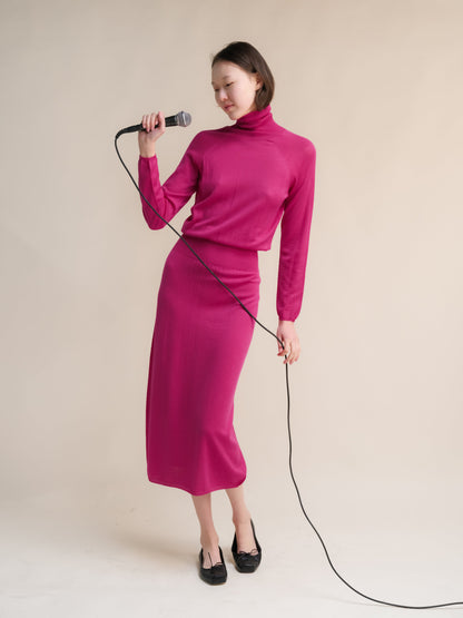 Model wearing magenta 3D-Knit Extra Fine Merino Wool Dress with a turtleneck, holding a microphone.