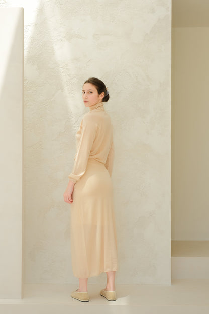 Beige 3D knit merino wool dress worn by a model standing sideways against a light textured wall