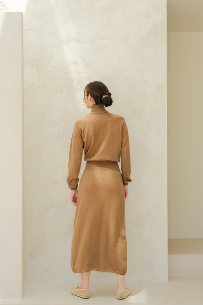 Back view of a model in camel brown knit dress with matching long skirt, hair in a bun.
