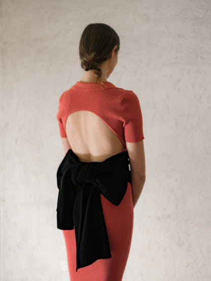 Back view of coral open-back knit dress with short sleeves and a black wrap tied at the waist.