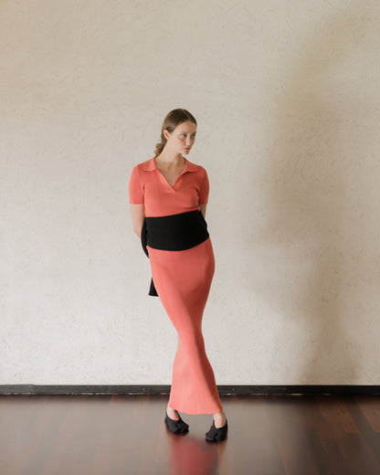 Full-length view of a model in a coral open-back knit dress with a wide black wrap at the waist.