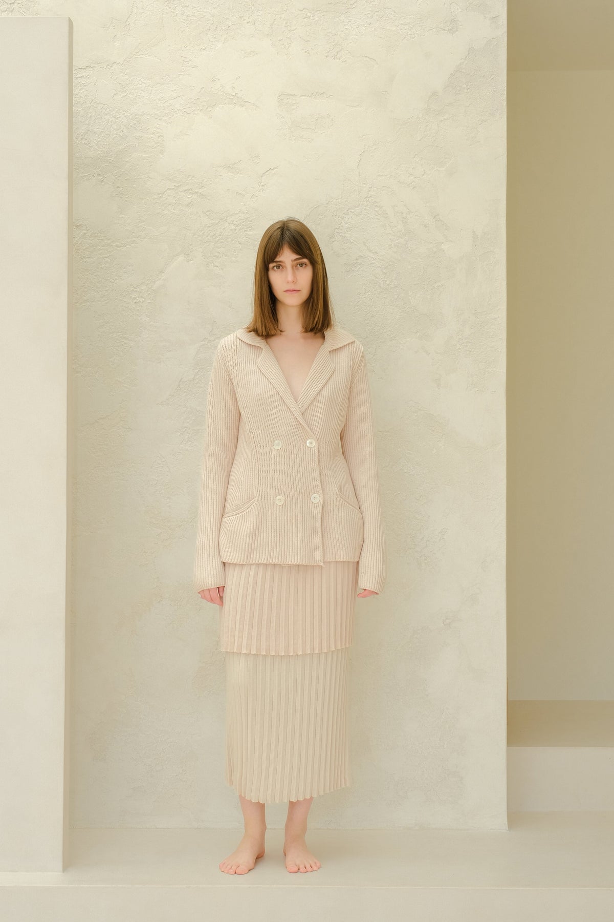 Model wearing a beige Fine Cotton Plissé Long Skirt with a matching double-breasted knit blazer