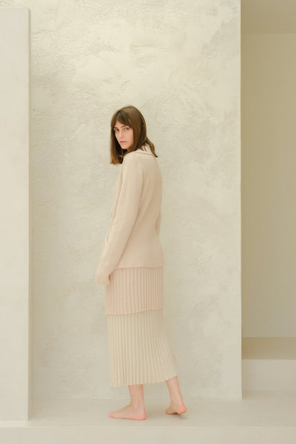 Side view of a model in a beige Fine Cotton Plissé knit ensemble with a long pleated skirt