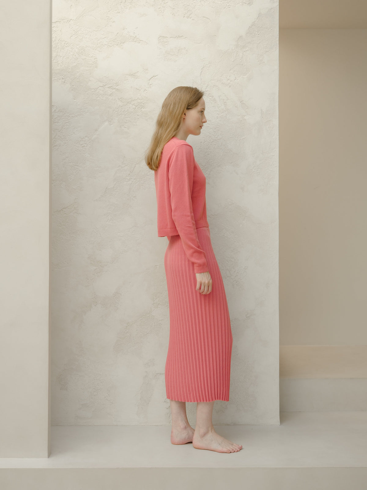 Side view of a model in a rose pink 3D Knit Fine Cotton Plissé Long Skirt with a cropped matching sweater.
