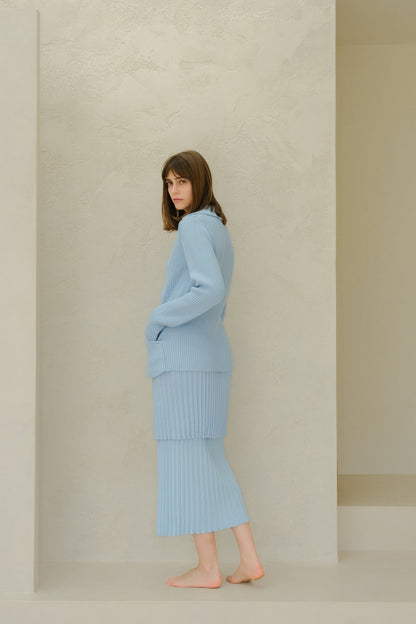 Side view of a model wearing a light blue Fine Cotton Plissé Long Skirt with a matching knit sweater in a neutral studio setting.